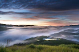 A panoramic view of a misty mountain range with olive and dark green tones at dawn.