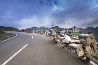 Motorcyclists gathered under a cloudy sky ready for a group ride on winding mountain roads.