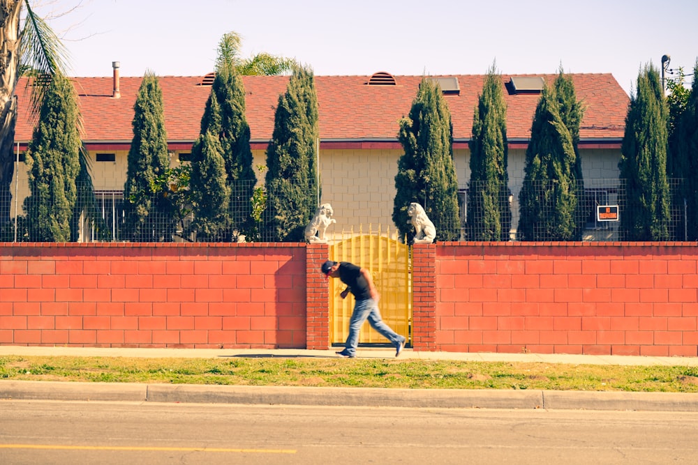 a man walking down a street past a red brick fence