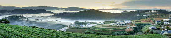 A panoramic view of the misty Gorthan area showcasing lush greenery and peaceful farmhouse plots.