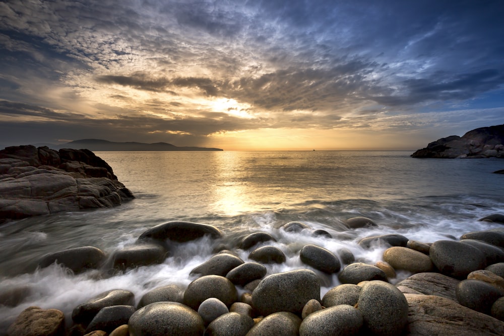 the sun is setting over the water and rocks