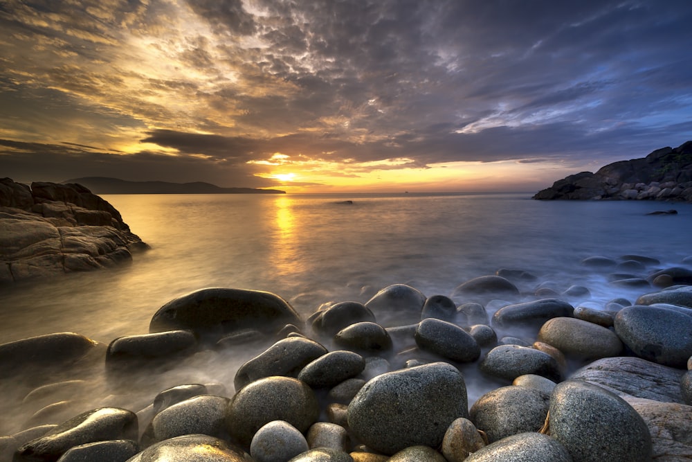 the sun is setting over the water and rocks