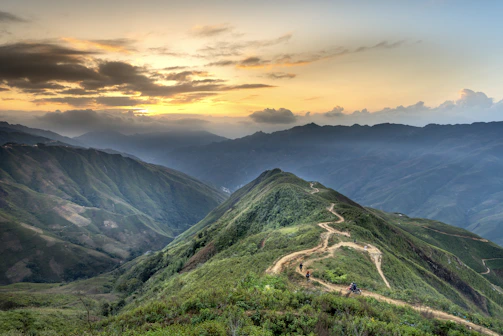 A scenic photo of a sunset viewed from a mountain trail with footprints in the dirt path.