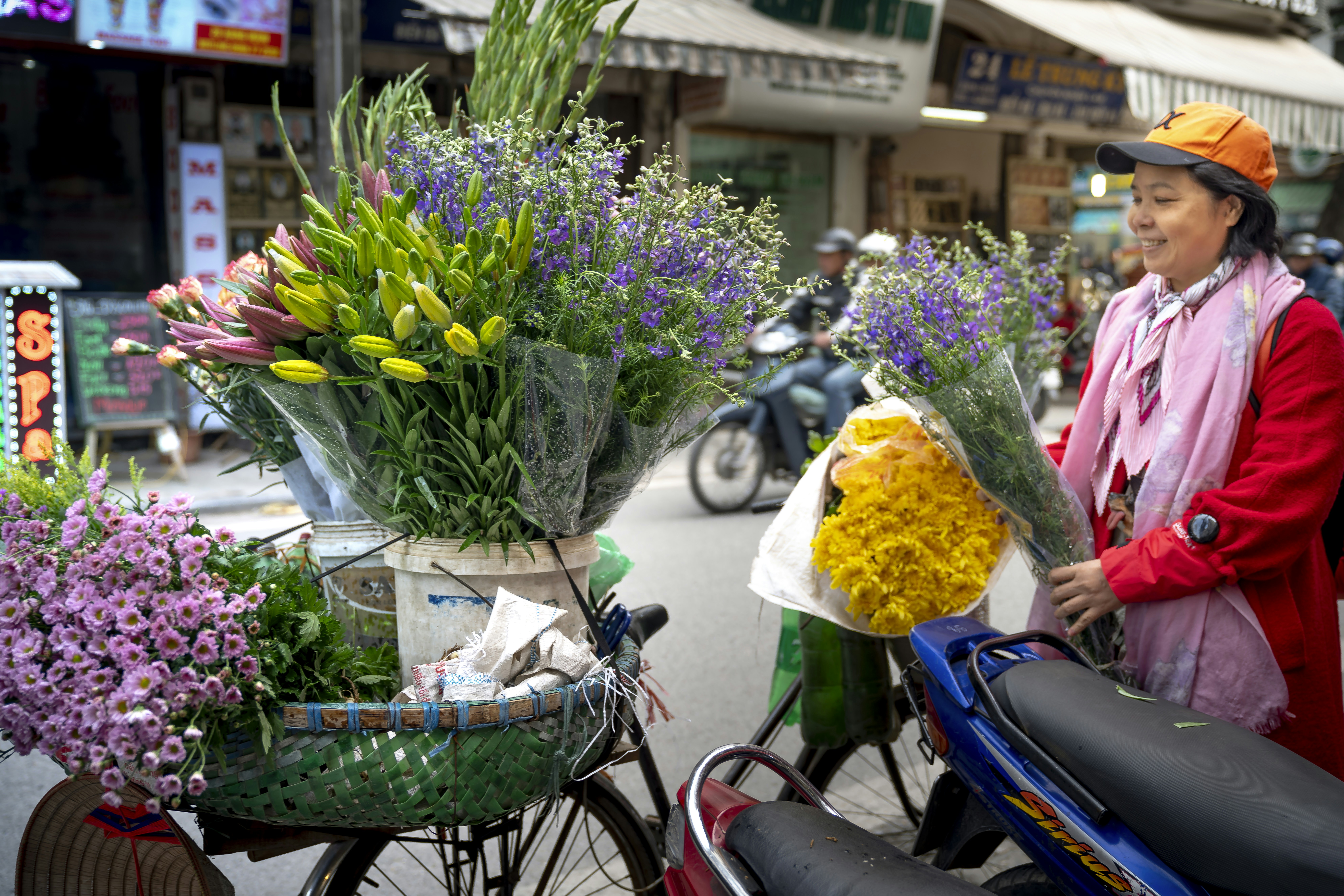 a woman pushing a bicycle with a basket full of flowers