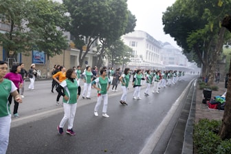 a group of people in green shirts and white pants marching down a street