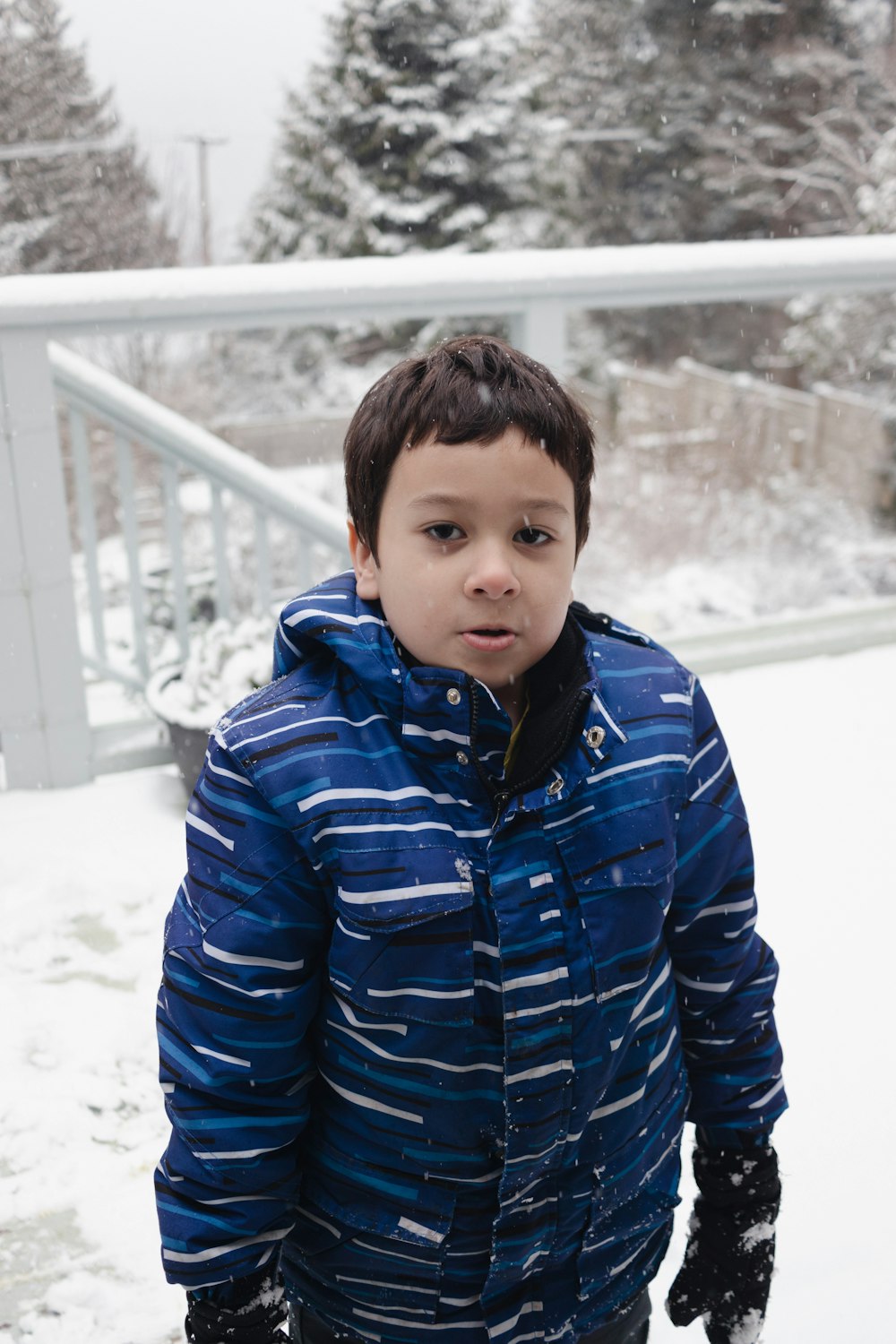 a young boy standing in the snow wearing a blue jacket