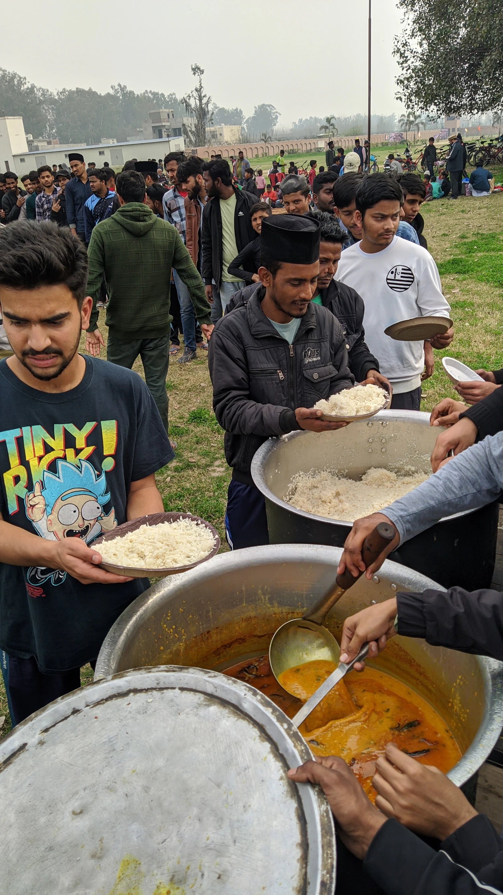 Volunteers serving a hot meal from large pots into steel plates