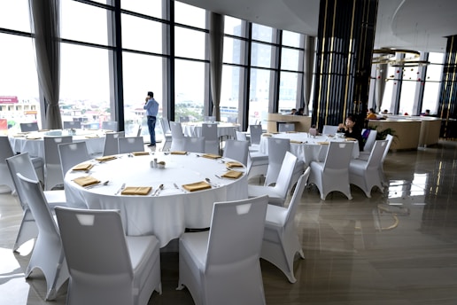 a room filled with lots of white tables and chairs