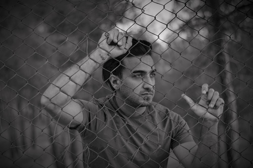 a man standing behind a fence holding a cigarette