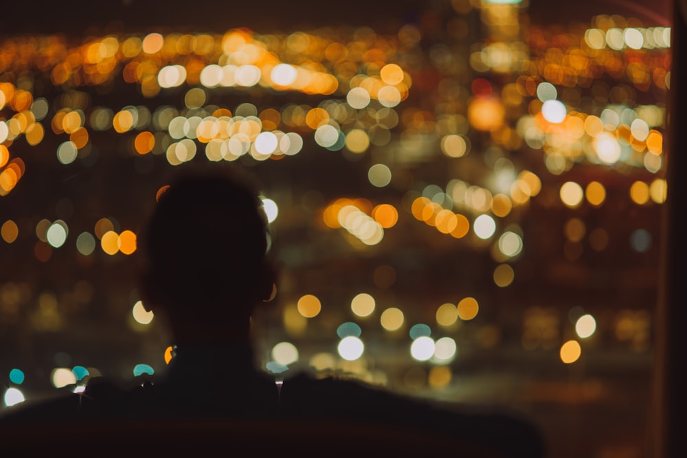 a person looking out a window at a city at night