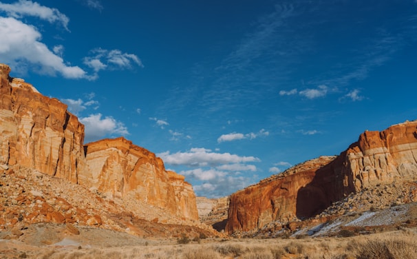 A vast desert landscape with dramatic red rock formations under a bright blue sky.