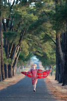A joyful person wearing a vibrant, patterned scarf while walking through a sunlit urban street.