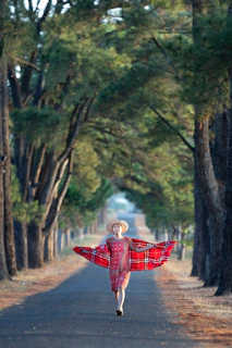 A joyful person wearing a vibrant, patterned scarf while walking through a sunlit urban street.