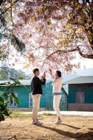 A candid shot of a couple laughing under a blooming cherry blossom tree.