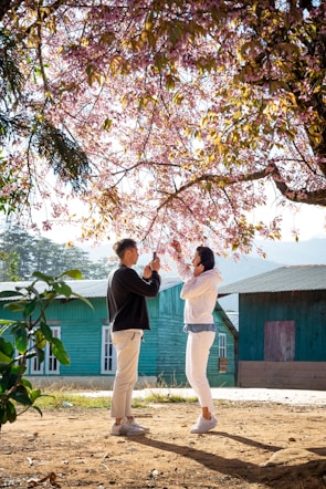 A candid shot of a couple laughing under a blooming cherry blossom tree.