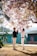 A smiling young couple standing in front of cherry blossoms in Tokyo.