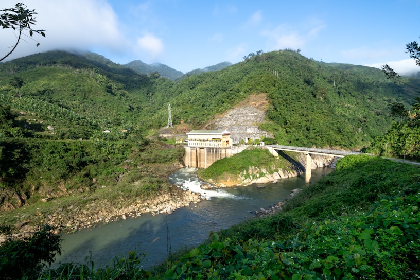 A serene river flowing through a lush green valley with a small hydroelectric dam.