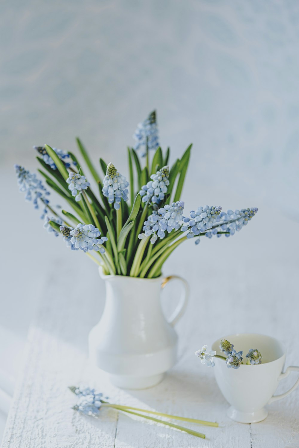 a white vase filled with blue flowers next to a cup