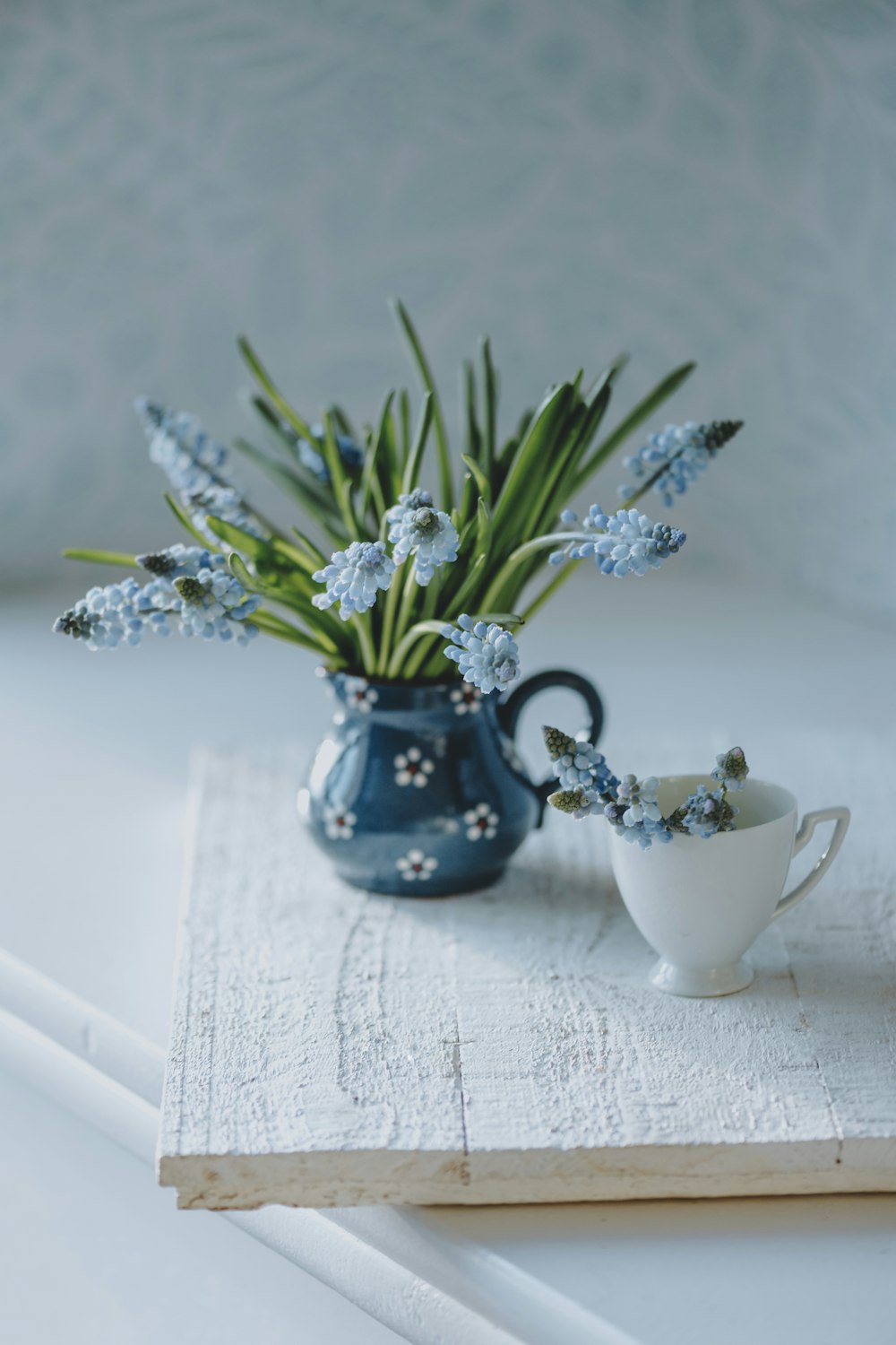 a blue vase filled with blue flowers next to a white cup