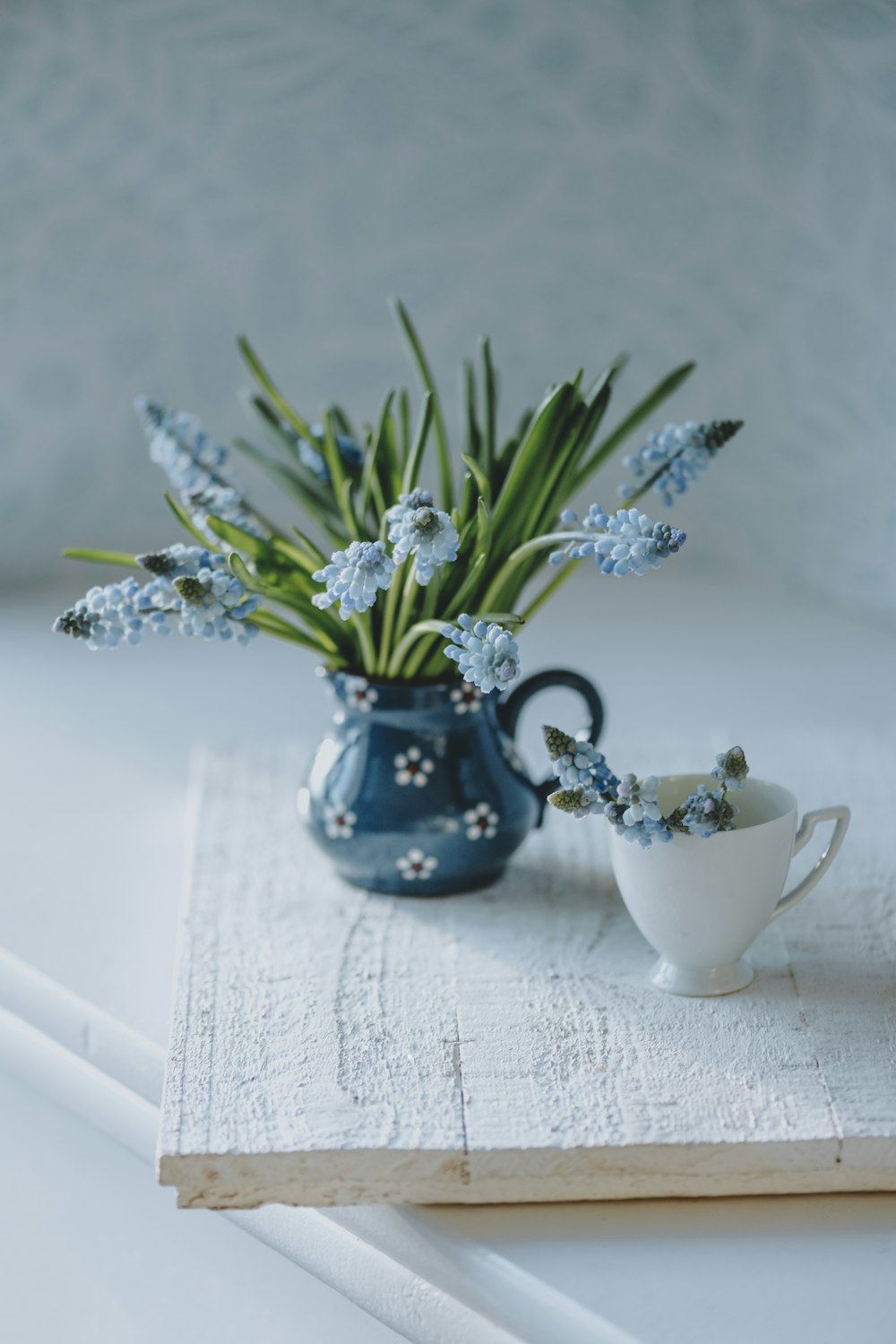 um vaso azul cheio de flores azuis ao lado de um copo branco