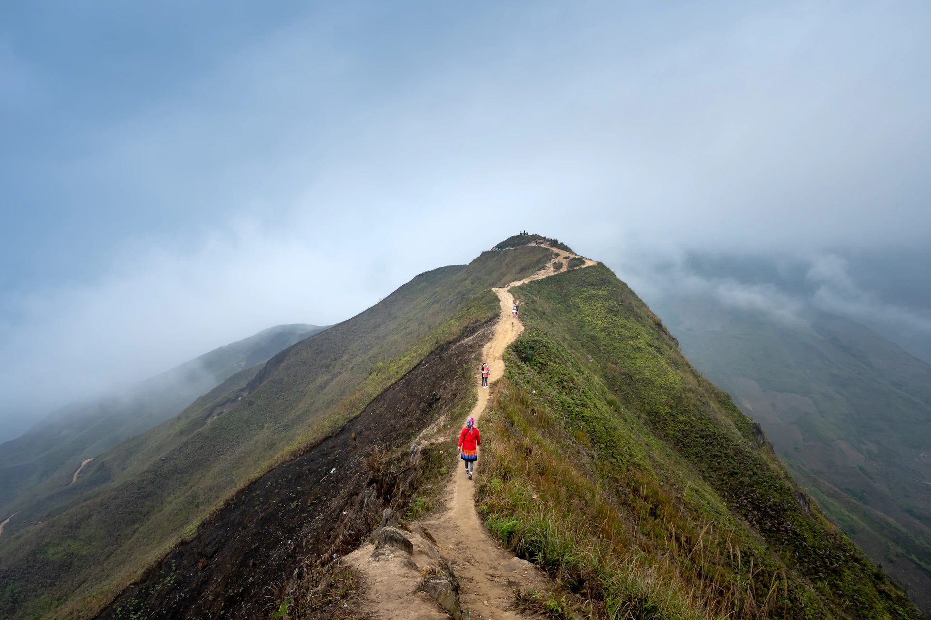 Adventurers trekking along a winding mountain trail with the Chimborazo volcano towering in the background, bathed in warm equatorial sunlight.