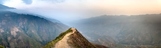 A lone traveler standing on a mountain ridge overlooking the misty valleys of Himachal Pradesh at sunrise.