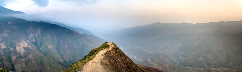 A lone traveler standing on a mountain ridge overlooking the misty valleys of Himachal Pradesh at sunrise.