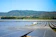 A vast field of solar panels arranged in rows, surrounded by lush greenery and set against a backdrop of rolling hills and a clear blue sky. The solar panels are evenly distributed, indicating a large-scale solar power plant.