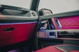 A luxurious car interior with red quilted leather upholstery and reflective metal accents. The door panel includes intricate stitching and multiple controls. Ambient lighting in shades of blue enhances the premium feel.