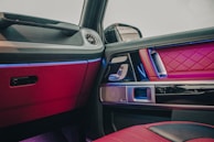 A luxurious car interior with red quilted leather upholstery and reflective metal accents. The door panel includes intricate stitching and multiple controls. Ambient lighting in shades of blue enhances the premium feel.