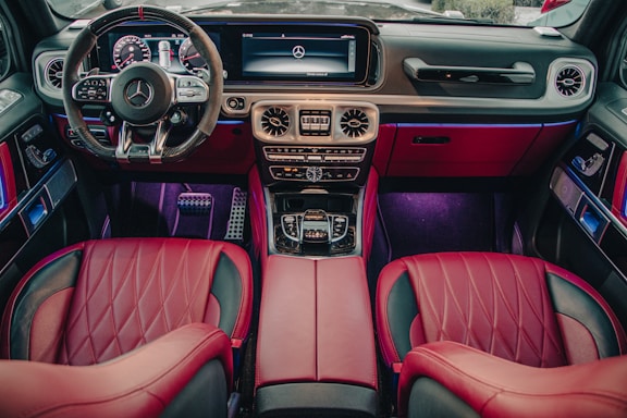 This image depicts the luxurious interior of a high-end car, featuring red leather seats, a sophisticated dashboard with a digital display, a multifunctional steering wheel, and ambient lighting. The design is modern and sleek, emphasizing comfort and style.