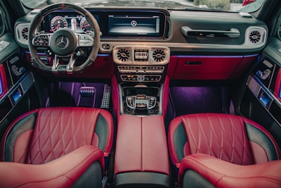This image depicts the luxurious interior of a high-end car, featuring red leather seats, a sophisticated dashboard with a digital display, a multifunctional steering wheel, and ambient lighting. The design is modern and sleek, emphasizing comfort and style.
