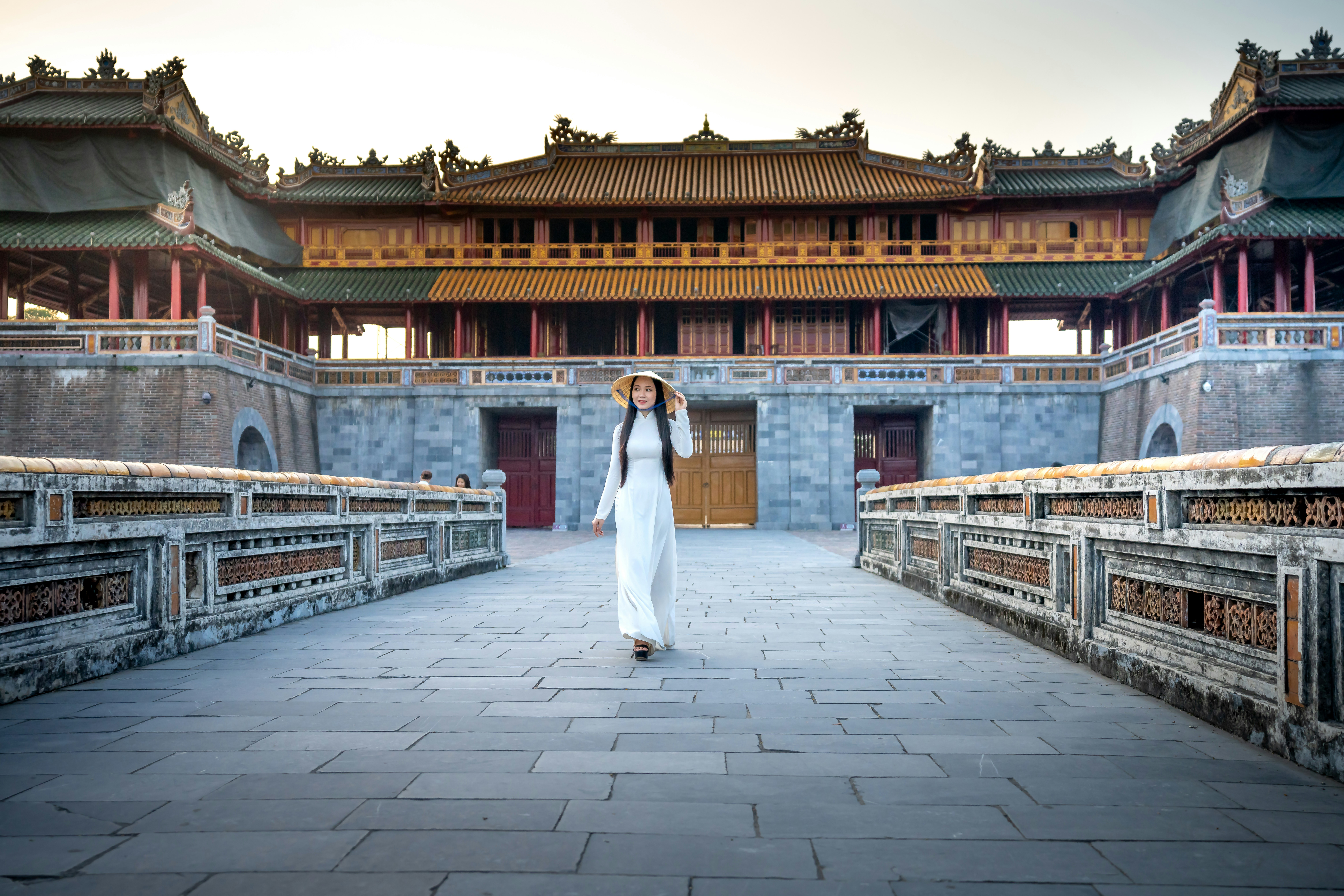 a woman in a white dress walking across a bridge
