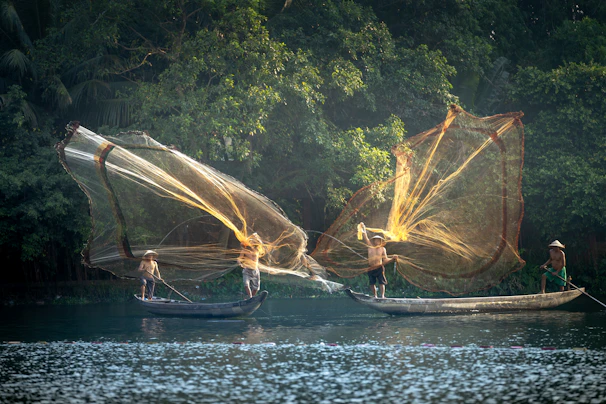 A candid shot of fishermen casting nets at dawn on a misty lake in Southeast Asia.
