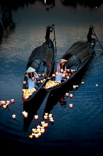 Traditional boats on a Hoi An river at dusk with locals placing lanterns in the water