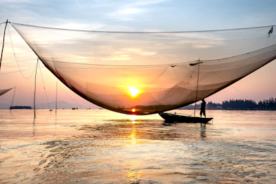 A serene fishing boat at dawn, casting nets over calm waters.