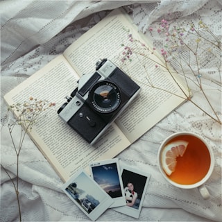 A travel journal open beside a steaming cup of tea, with postcards and a camera nearby.