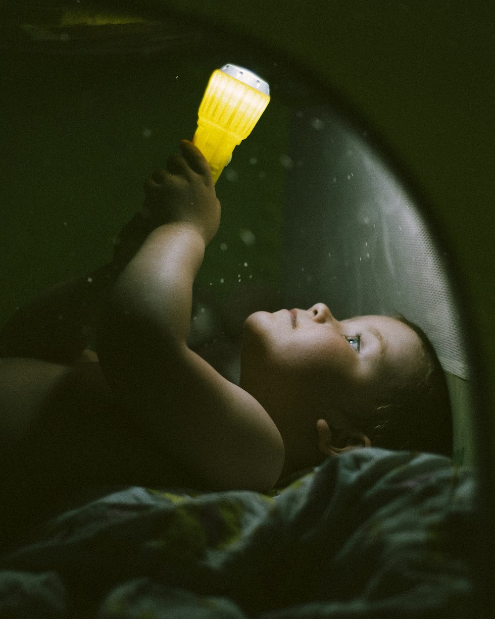 a young boy laying in bed holding a yellow light