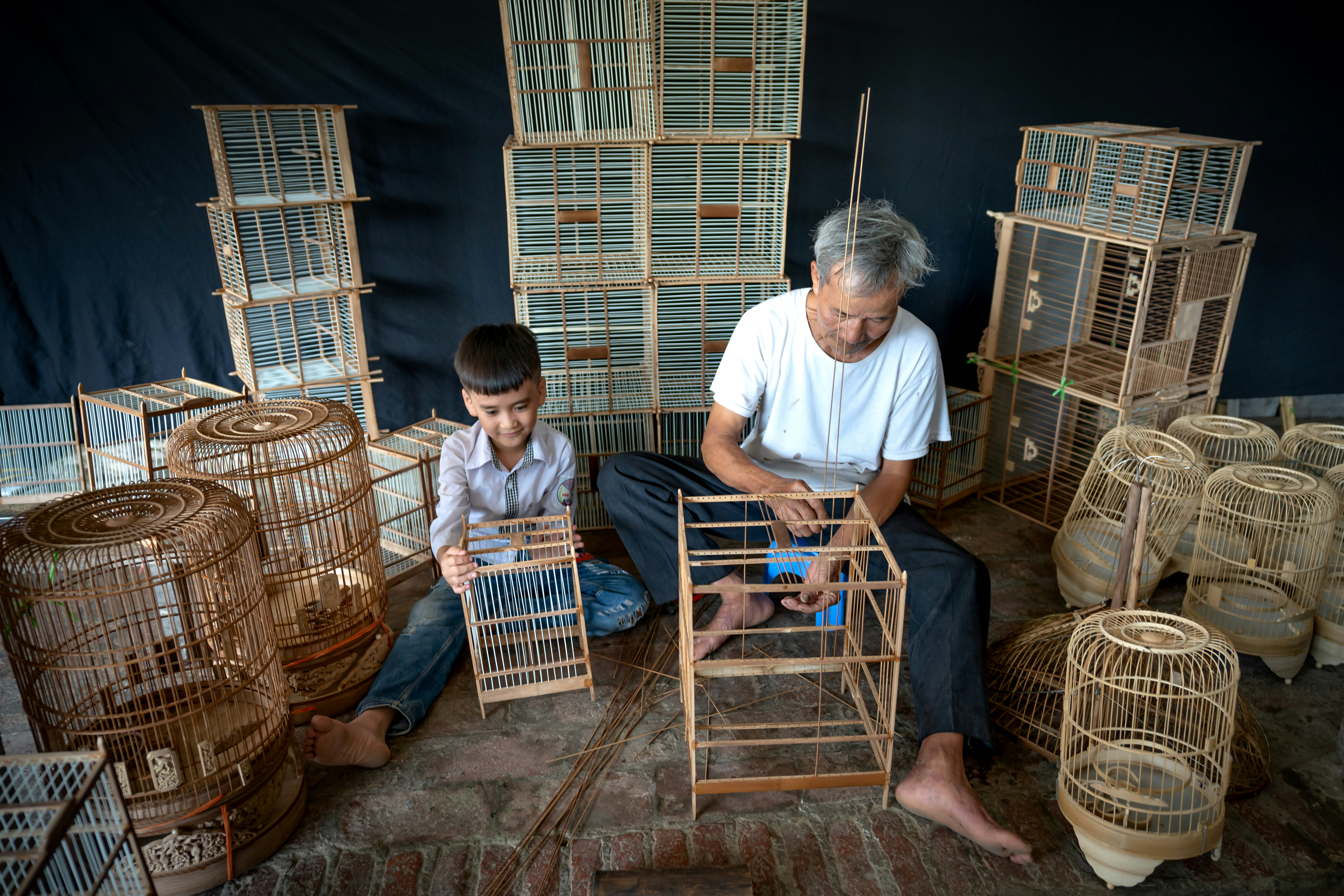a man sitting next to a boy in front of bird cages