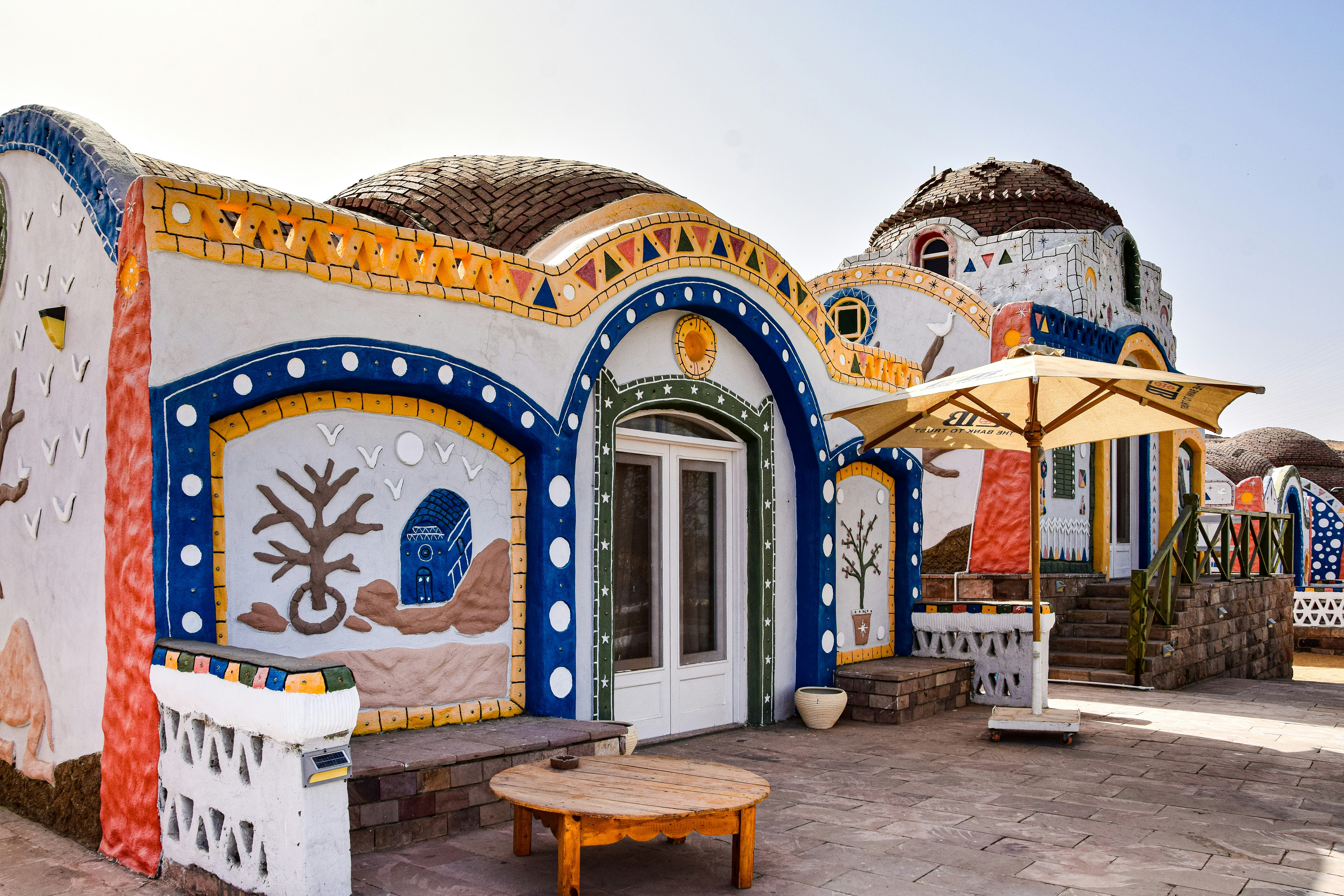 a colorfully painted building with a wooden table and umbrellas, Aswan, Egypt.