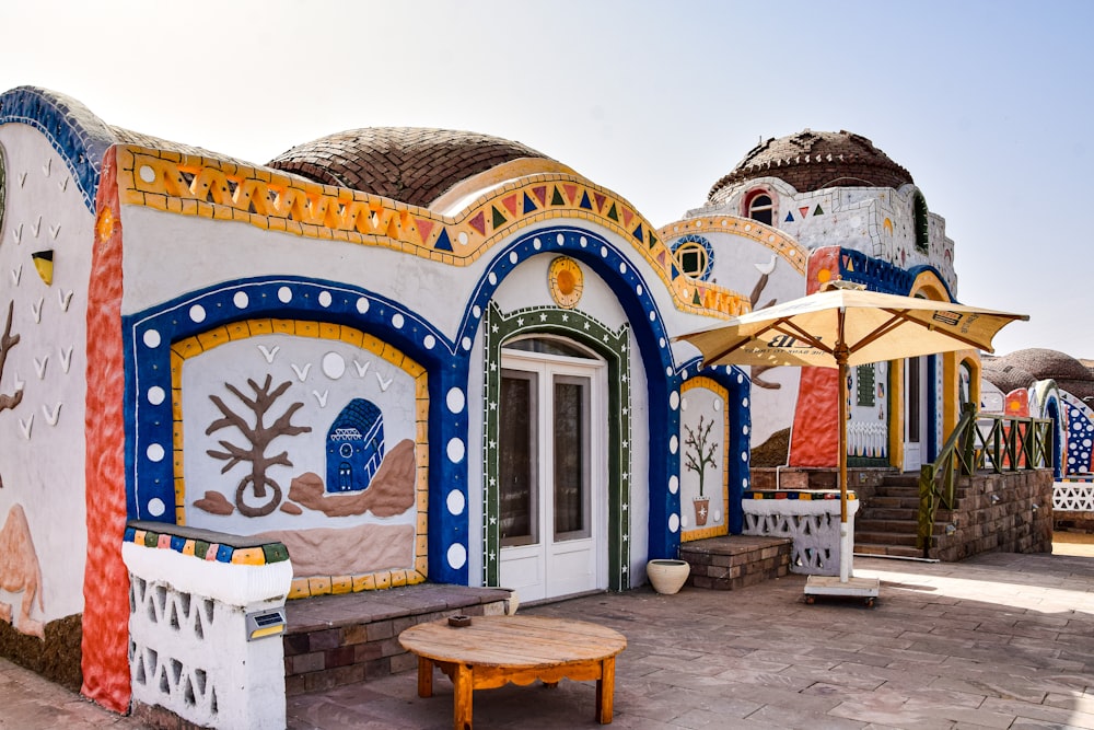 a colorfully painted building with a wooden table and umbrellas