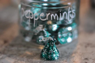 Close-up of colorful mint candies spilling from a glass jar onto a wooden table.