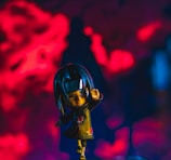 A stylized figurine of a character with intense expression, dressed in a dark cloak with red cloud patterns, set against a vibrant red and dark blue background. The character is depicted in a dynamic pose, suggesting motion or action.
