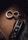 A luxury car key fob is placed on a wooden surface alongside a set of metallic rings in a figure-eight formation. Partially visible underneath is a piece of currency, suggesting a sense of affluence.