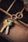 A close-up view of a set of keys attached to a unique keyring with an intertwined double ring design. The keys and keyring are placed on the edge of a wooden compartmentalized organizer, with different sections visible and a piece of torn paper partially seen in the upper right corner.