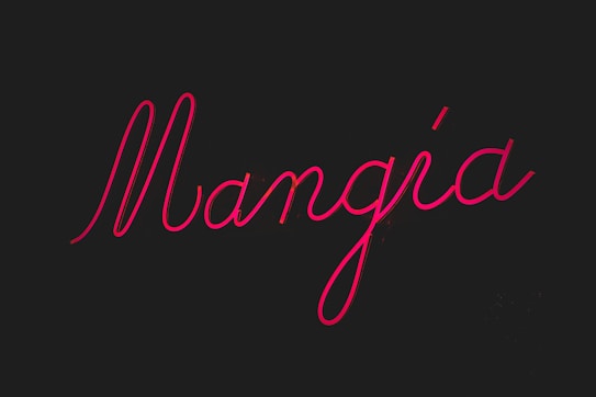 Neon pink cursive text spells out the word 'Mangia' against a dark black background, creating a striking and bold visual contrast.