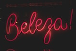 Bright pink neon sign displaying the word 'Beleza' against a dark background. The glowing letters have a cursive style, creating an eye-catching and lively appearance.
