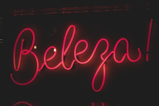 Bright pink neon sign displaying the word 'Beleza' against a dark background. The glowing letters have a cursive style, creating an eye-catching and lively appearance.