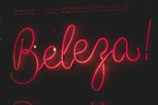 Bright pink neon sign displaying the word 'Beleza' against a dark background. The glowing letters have a cursive style, creating an eye-catching and lively appearance.
