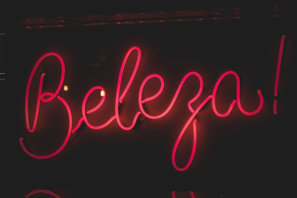 Bright pink neon sign displaying the word 'Beleza' against a dark background. The glowing letters have a cursive style, creating an eye-catching and lively appearance.